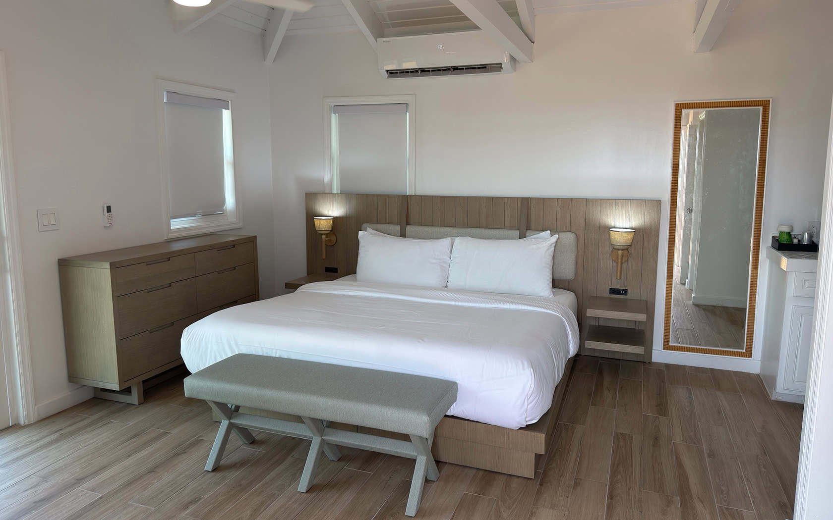 Hotel-style bedroom with a large bed, white linens, and a wooden headboard flanked by wall lamps and matching nightstands.